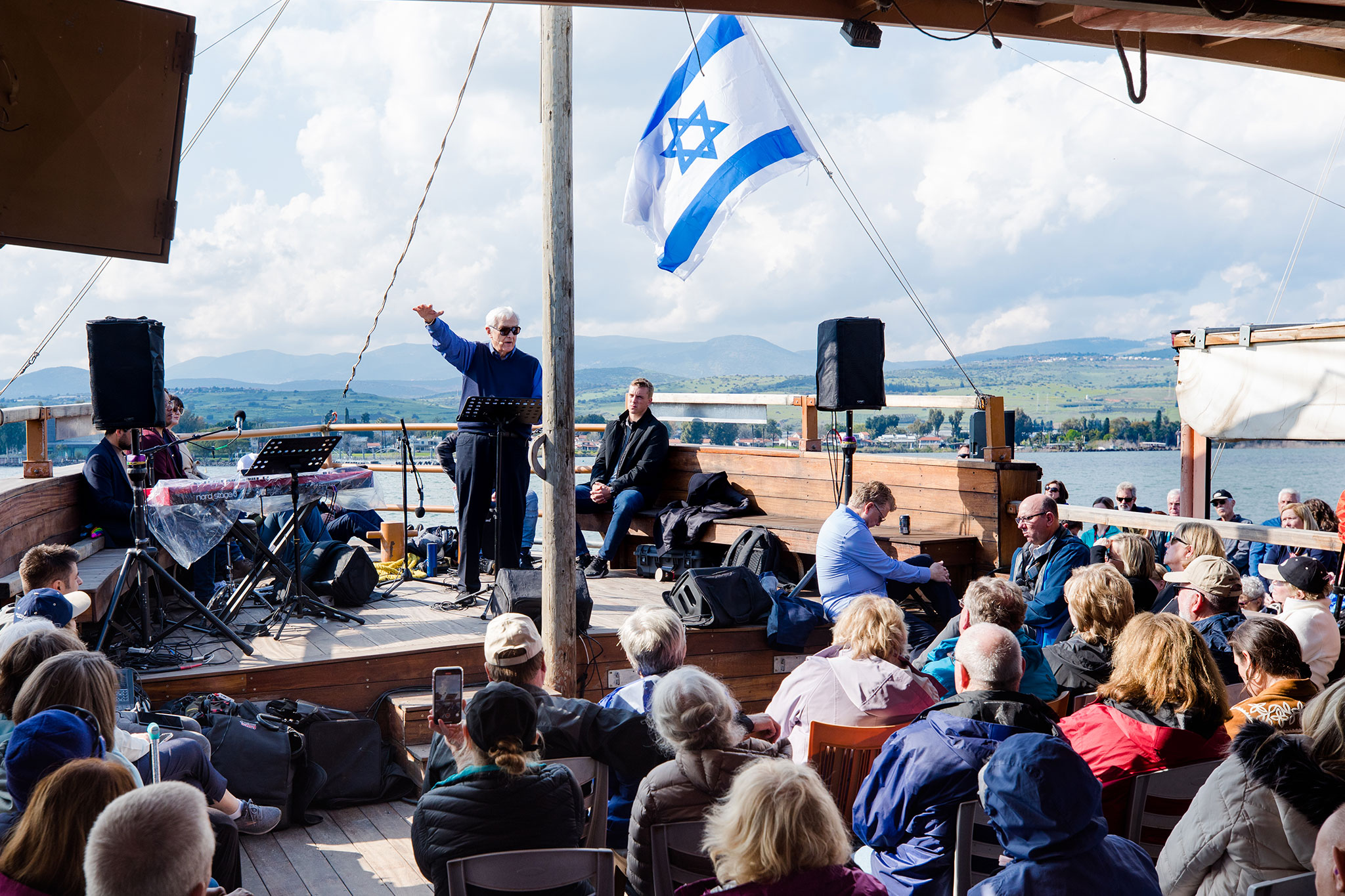 A speaker delivers a message to a group on a boat with an Israeli flag waving above.